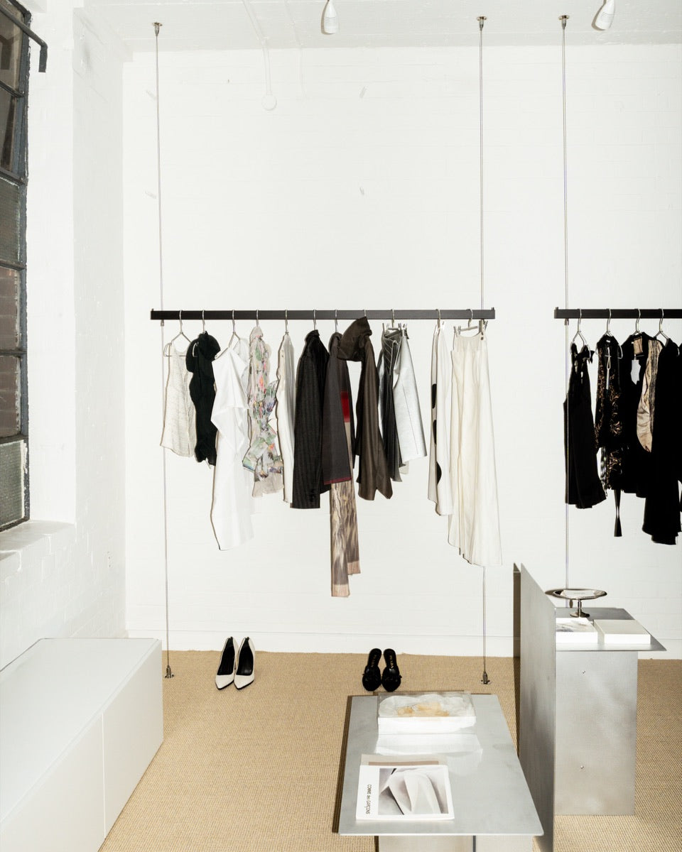 White-walled Mondō studio with suspended rails of black and cream garments and steel display tables.