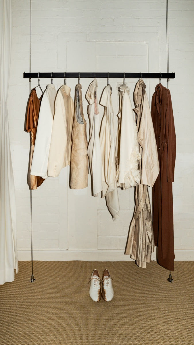Cream garments and shoes arranged along a steel rail in the Mondō studio.